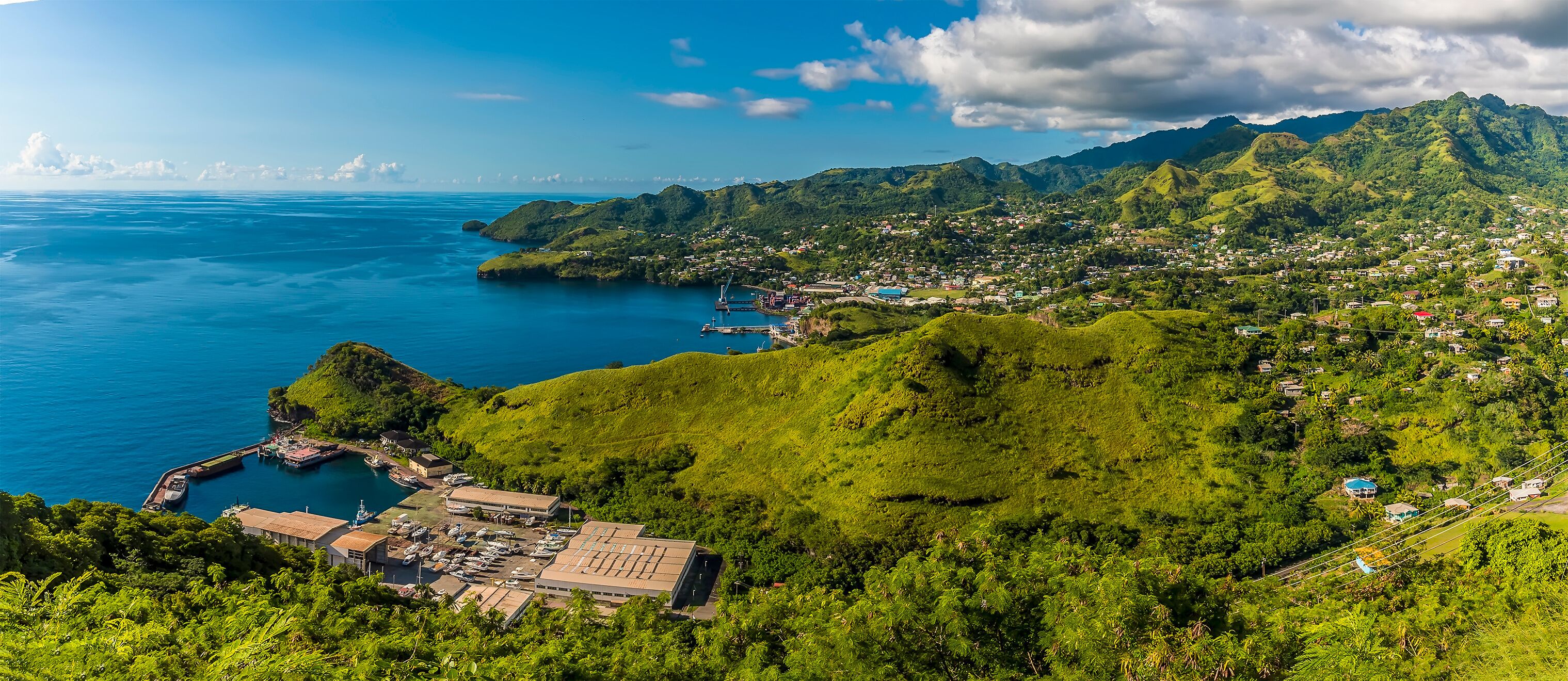 A coastal town with lush green hills, a marina, and a clear blue sea.