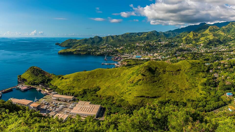 A coastal town with lush green hills, a marina, and a clear blue sea.