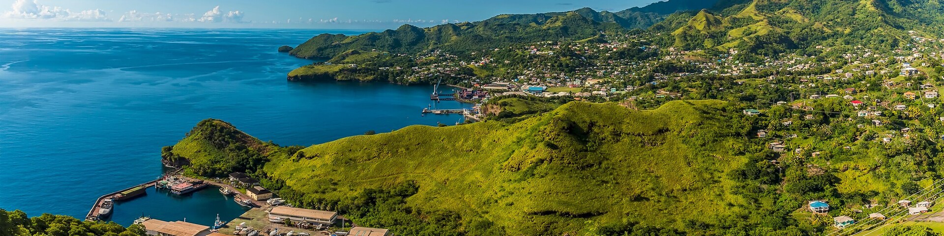 Uma cidade costeira com colinas verdejantes, um porto de iates e um mar azul cristalino.