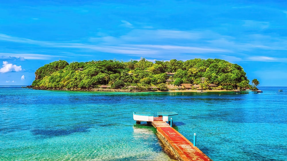 Une île tropicale aux eaux turquoise et limpides, avec une jetée qui y mène.