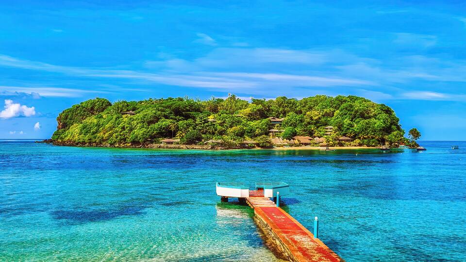 A tropical island with clear turquoise waters and a pier leading to it.