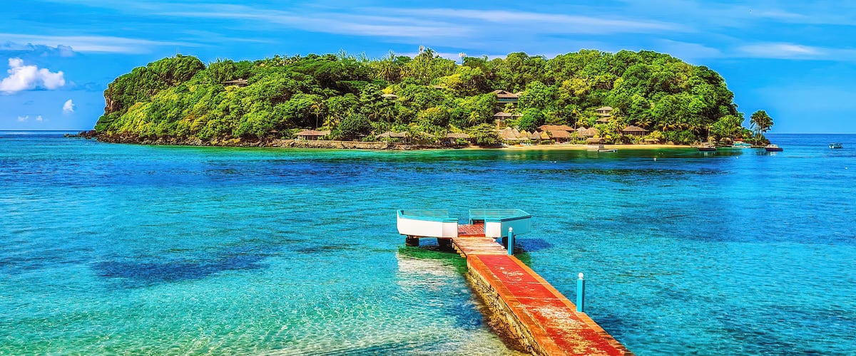 A tropical island with clear turquoise waters and a pier leading to it.