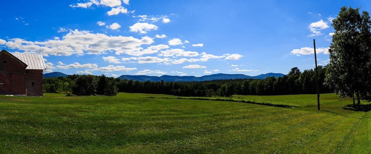 A red barn, green field, and mountains under a blue sky.