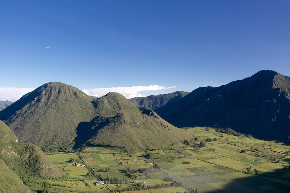 Paisagem montanhosa com vales verdejantes e casas dispersas.
