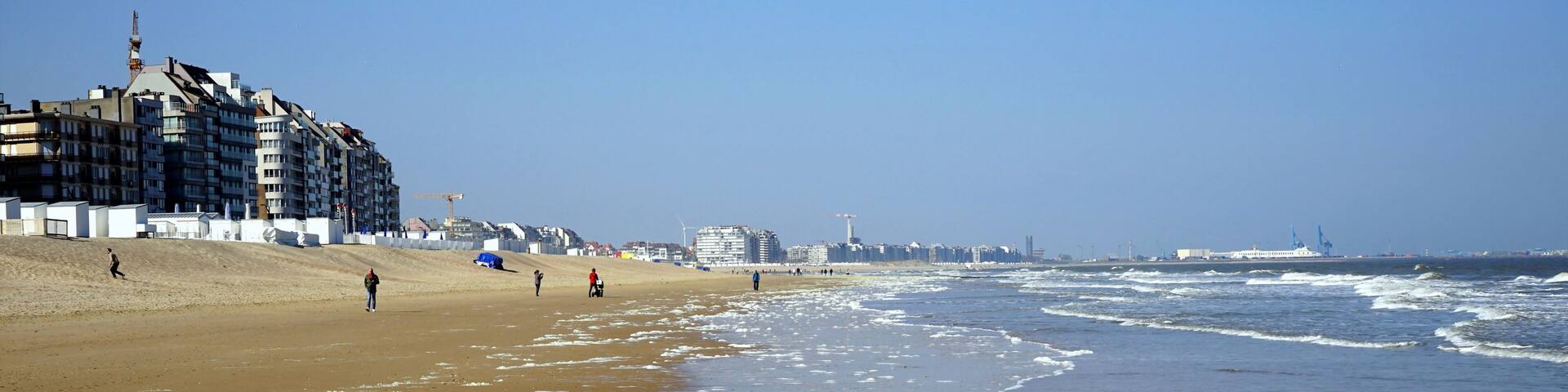 Brandung mit weißem Schaum am Strand der Nordsee mit Blick Richtung Zeebrügge bei blauem Himmel und Sonnenschein in Knokke-Heist bei Brügge in Westflandern in Belgien