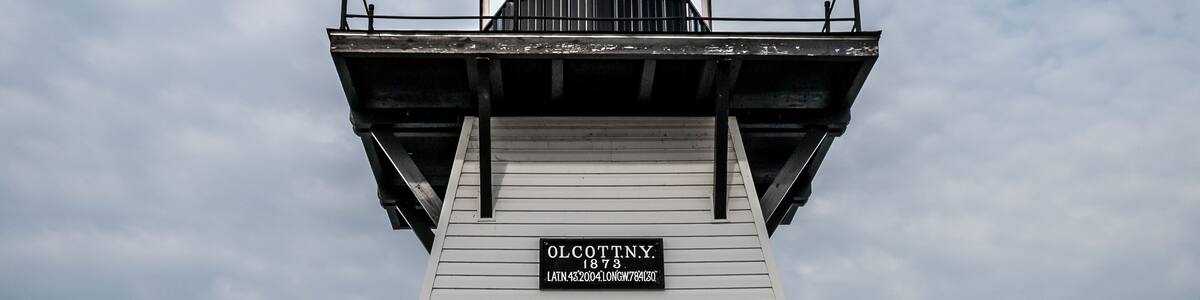 A white lighthouse with a sign reading 'OLCOTTNY 1873' and a door at the base.