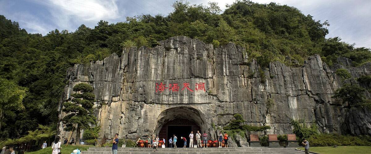 A large rock formation with a cave entrance, surrounded by lush greenery.