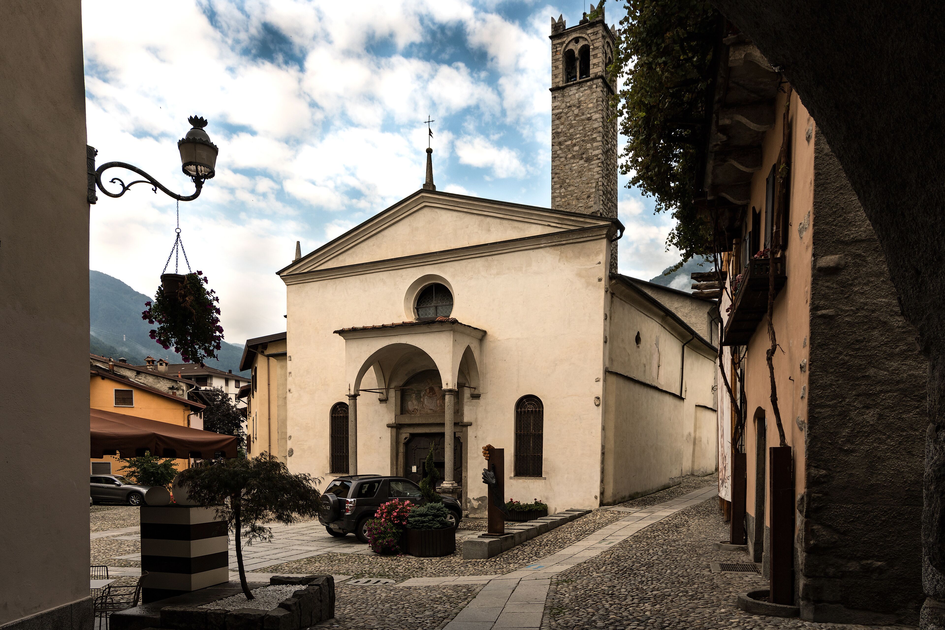 A church with a bell tower, a cobblestone street, and parked cars.