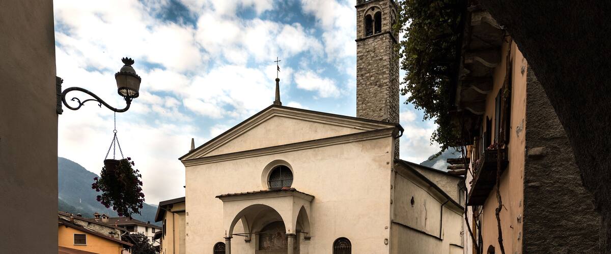 A church with a bell tower, a cobblestone street, and parked cars.