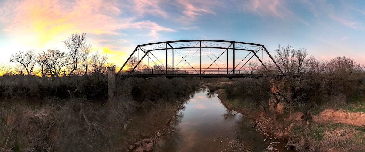 A metal bridge over a calm river at sunset.
