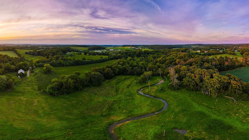 A lush green landscape with winding roads and fields, a sunset in the distance, and scattered buildings.