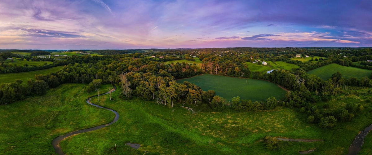 A lush green landscape with winding roads and fields, a sunset in the distance, and scattered buildings.
