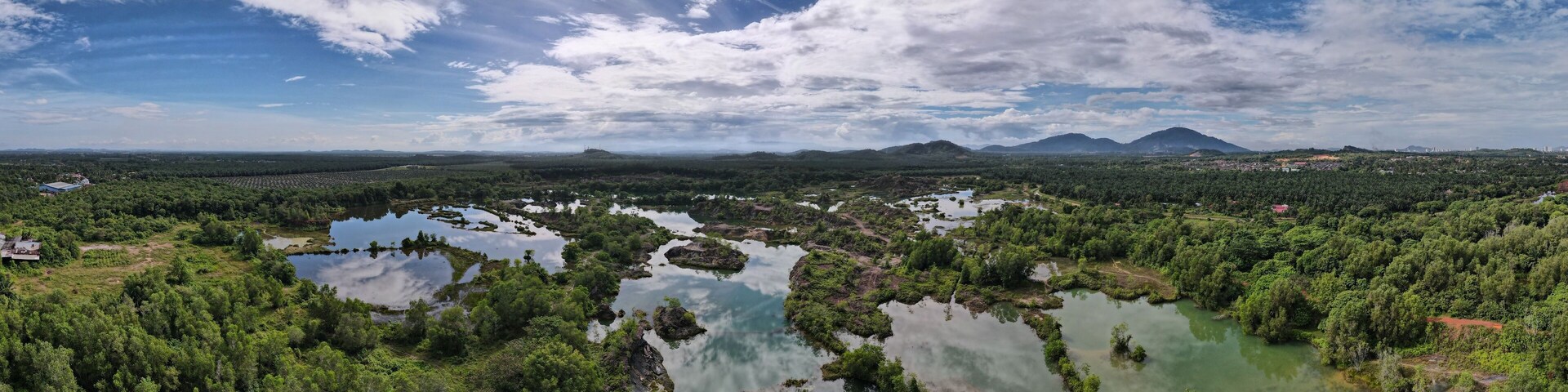 Un río serpentea por un bosque denso, con estanques dispersos y montañas lejanas, bajo un cielo parcialmente nublado.