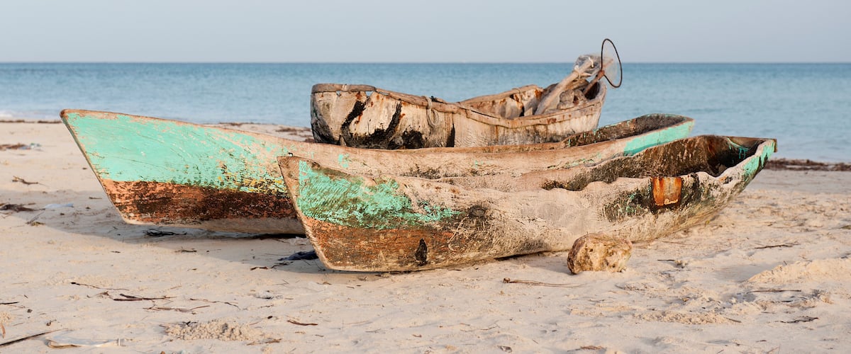 Two old, weathered boats on a sandy beach with the sea in the background.
