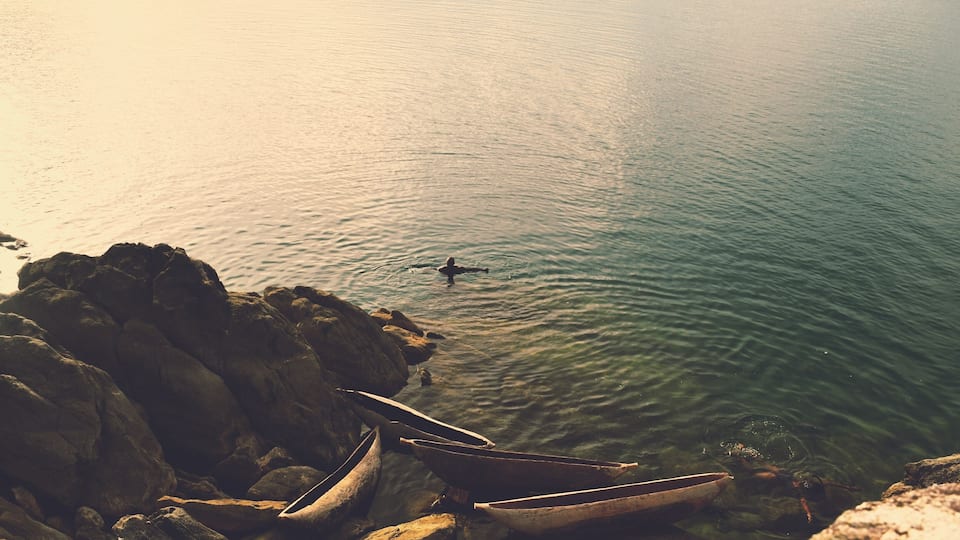 A rocky shoreline with several boats and a person swimming in the water.