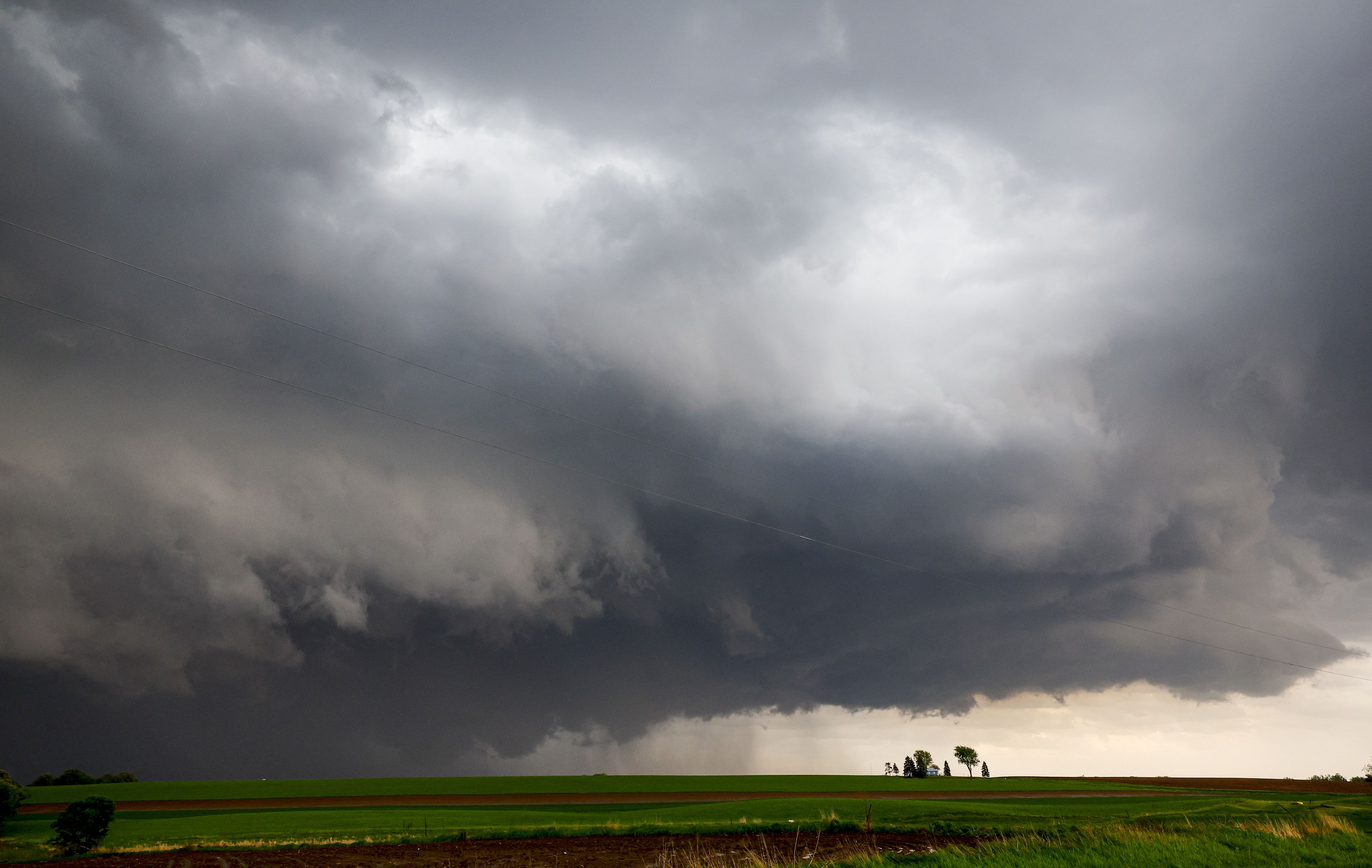 A stormy sky over a green field with a few trees and a small building.