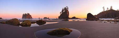 A coastal landscape with large rock formations, tide pools, and a sunset sky.