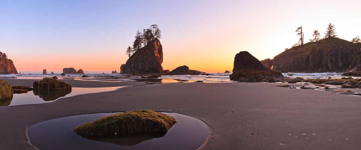A coastal landscape with large rock formations, tide pools, and a sunset sky.