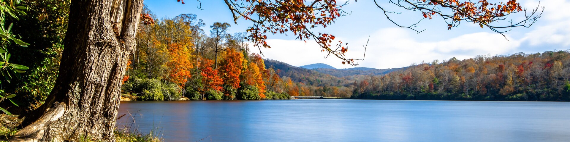 Um lago calmo rodeado por folhagem outonal e um céu limpo.