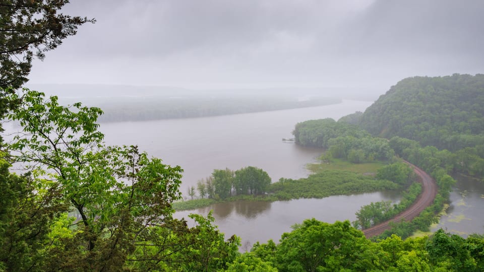 A river winding through a forested landscape with a railway track alongside it.