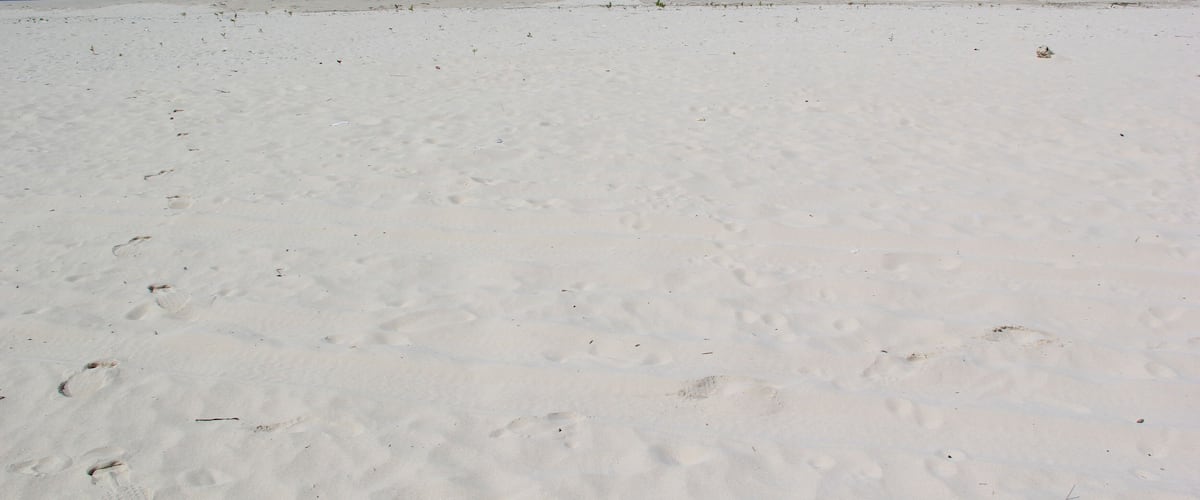 A white sandy beach with footprints and a boat in the water.