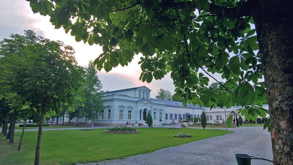Un bâtiment de style classique, doté d’une façade symétrique, entouré d’une pelouse bien entretenue et d’arbres.