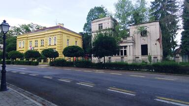A yellow building with a red roof, a white building with columns, and a street with yellow lines.
