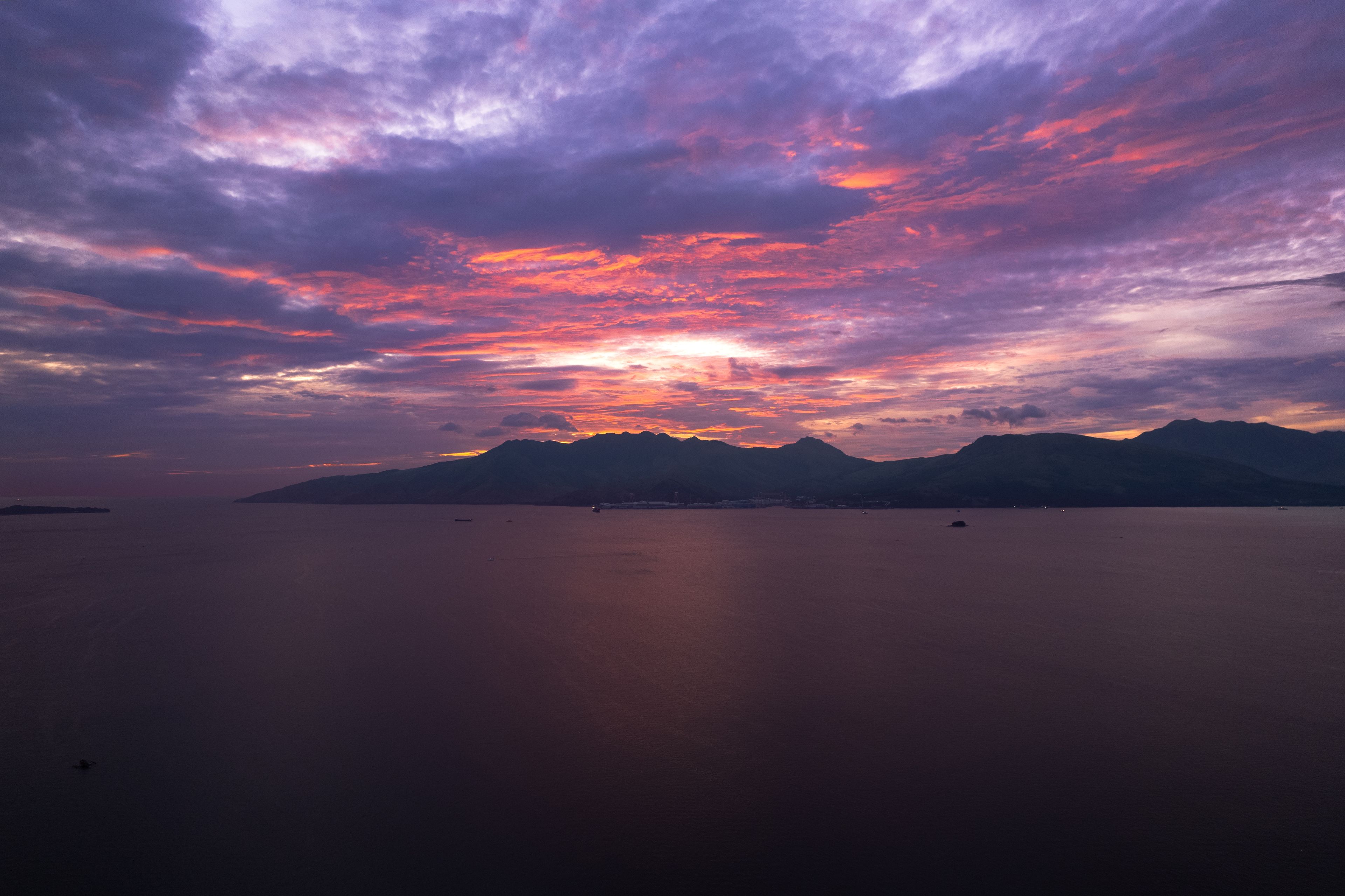 Un atardecer sobre un mar tranquilo con montañas a lo lejos.