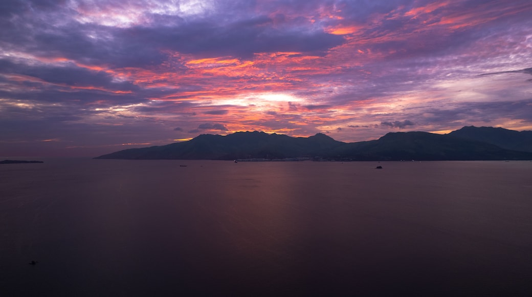 Un atardecer sobre un mar tranquilo con montañas a lo lejos.