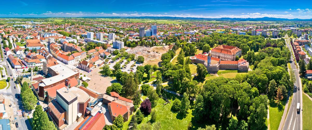 A panoramic view of a city with a mix of historical and modern architecture, surrounded by green parks and a river.