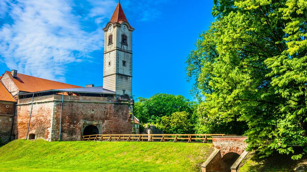 A historic building with a clock tower, surrounded by lush green trees and a clear blue sky.