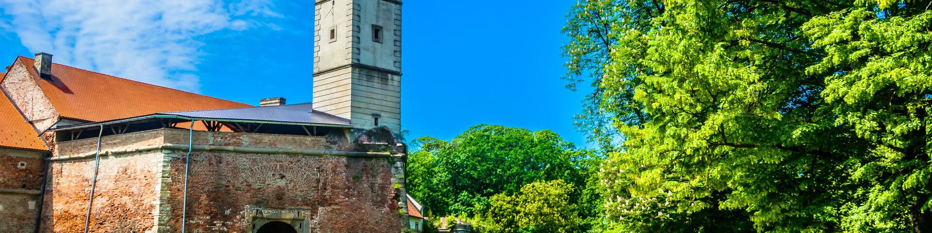 A historic building with a clock tower, surrounded by lush green trees and a clear blue sky.