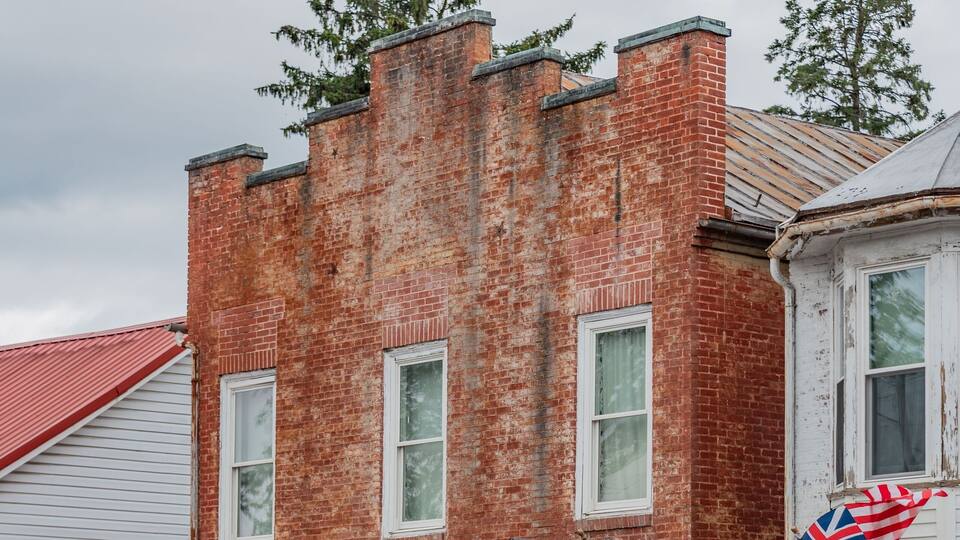 A red brick building with white trim and a porch. There are American flags and flowers on the porch.
