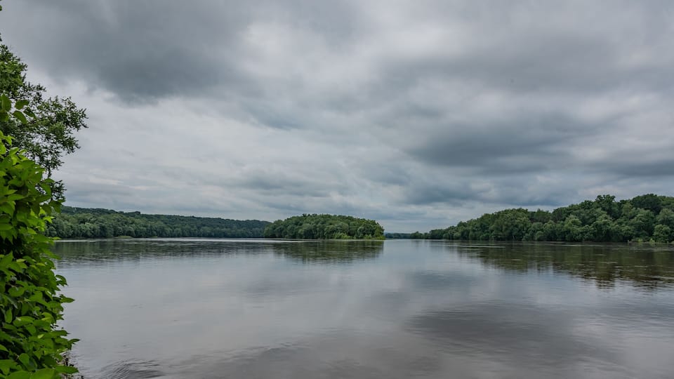 A calm river with dense green banks and overcast skies.