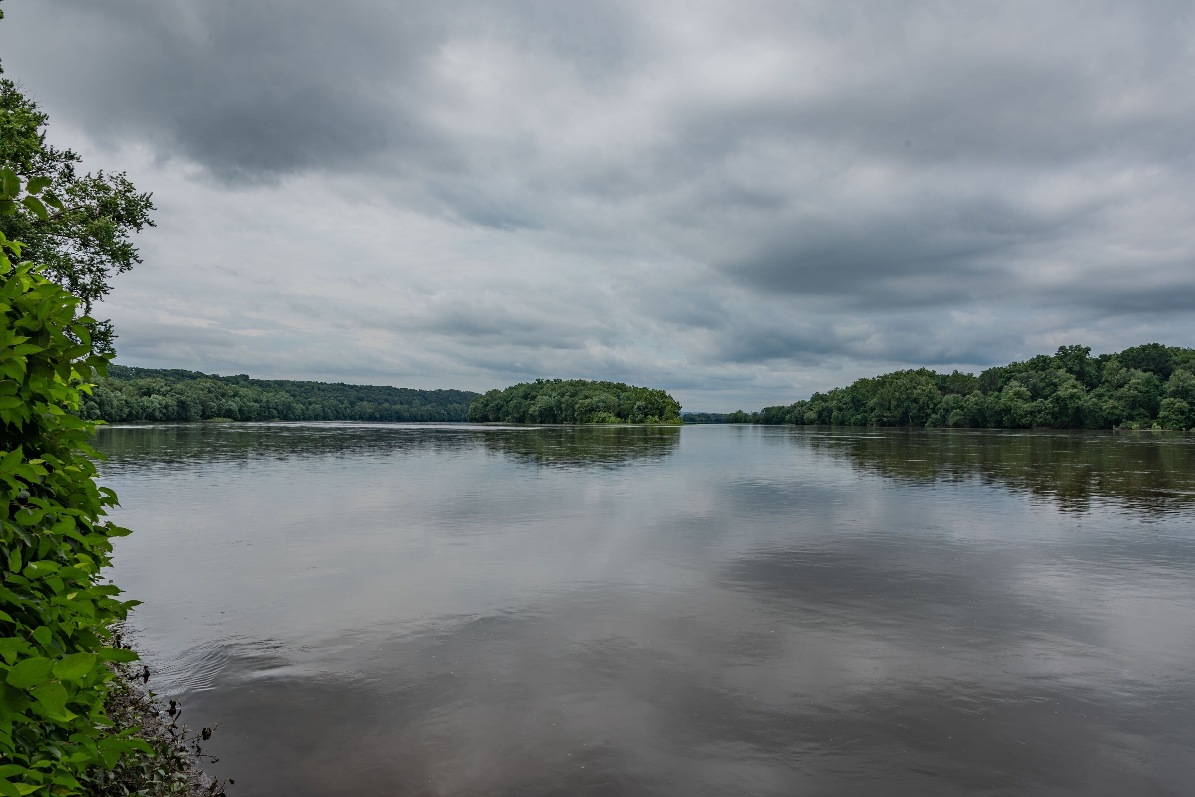 A calm river with dense green banks and overcast skies.