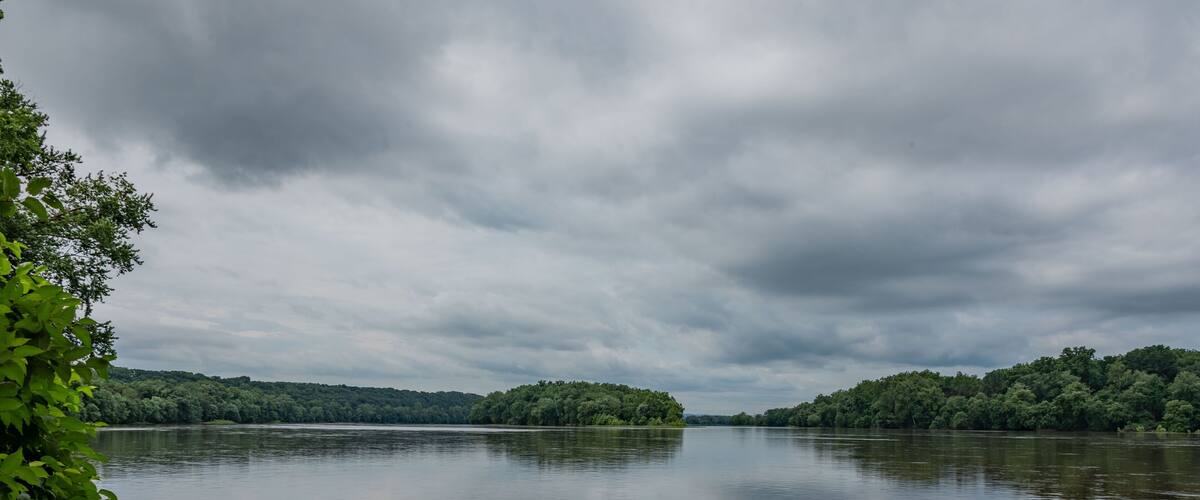 A calm river with dense green banks and overcast skies.