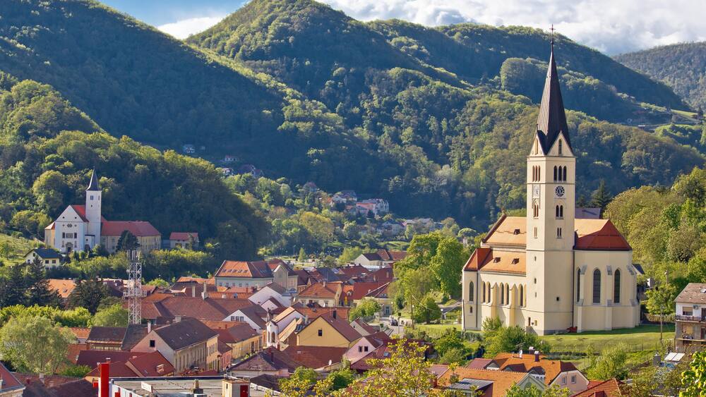 A town with a prominent church and a tall tower, surrounded by lush green hills.