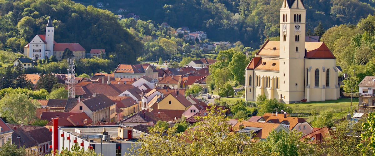 A town with a prominent church and a tall tower, surrounded by lush green hills.