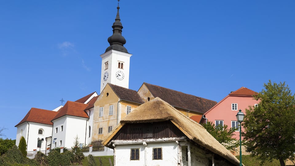 A church with a clock tower, a thatched-roof house, and colorful buildings.