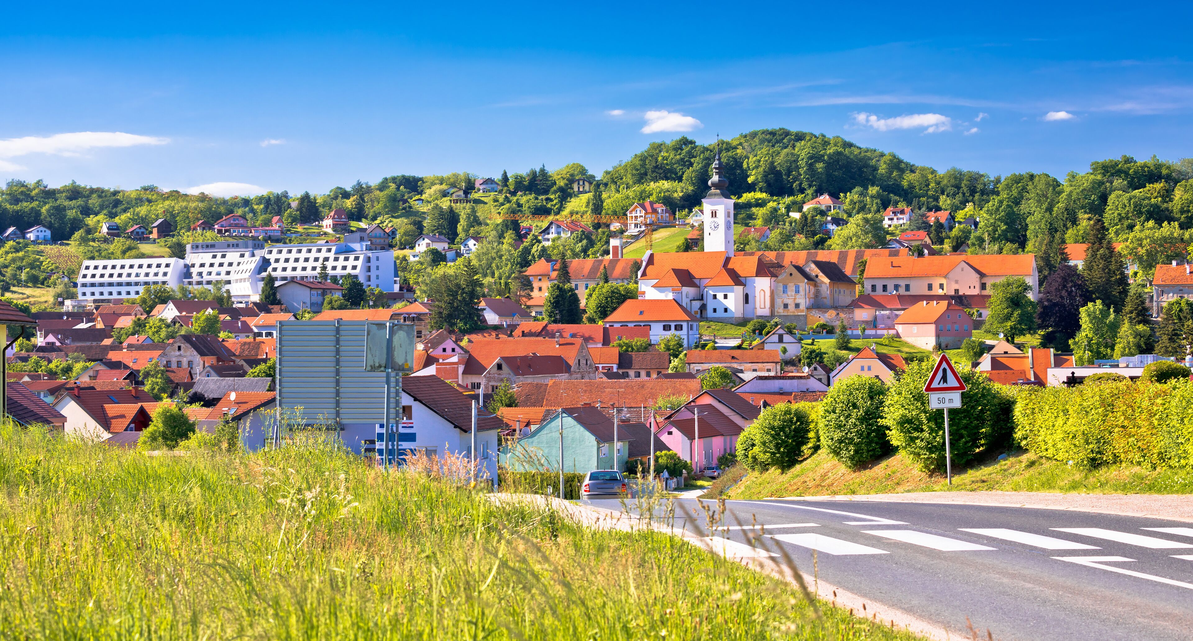 A town with red-roofed houses, a church, and a hill with greenery.