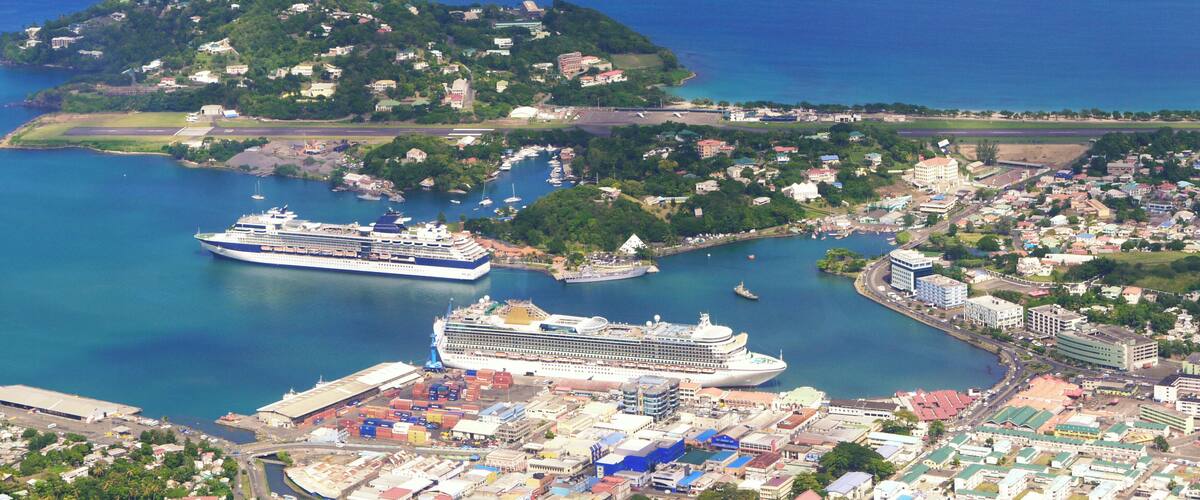 A coastal city with a cruise ship docked at a port, surrounded by residential buildings and a small island with a lighthouse.