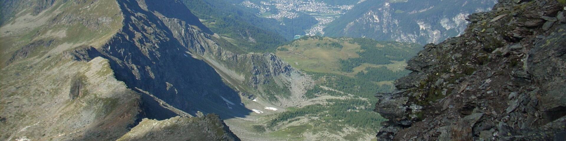 A mountainous landscape with a valley, rocky terrain, and distant snow-capped peaks.