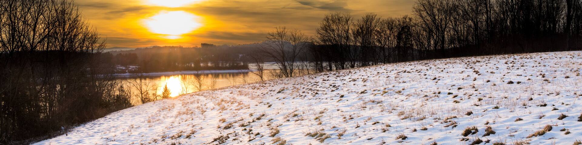 Panoramic view of a sunrise over Blue Marsh Lake with a snowy field in the foreground