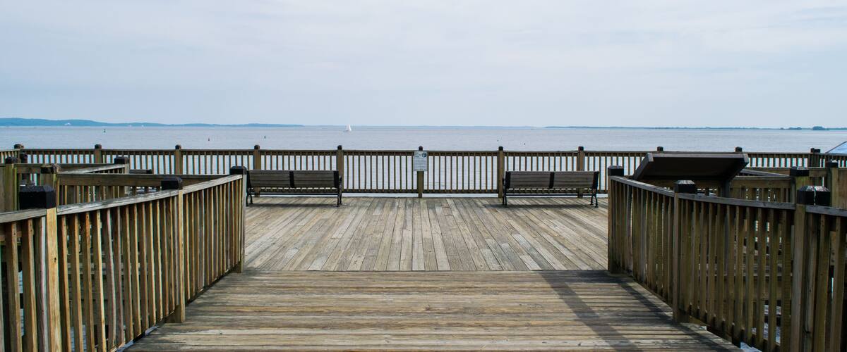 A wooden boardwalk leading to a body of water with benches and a railing.
