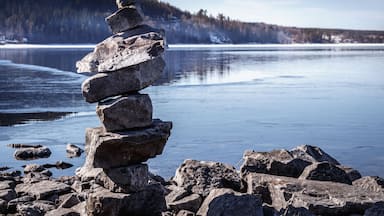 Una pila de rocas junto a un lago tranquilo con una colina boscosa al fondo.