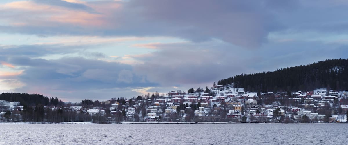 A snowy town by a body of water with a backdrop of mountains and a colorful sky.