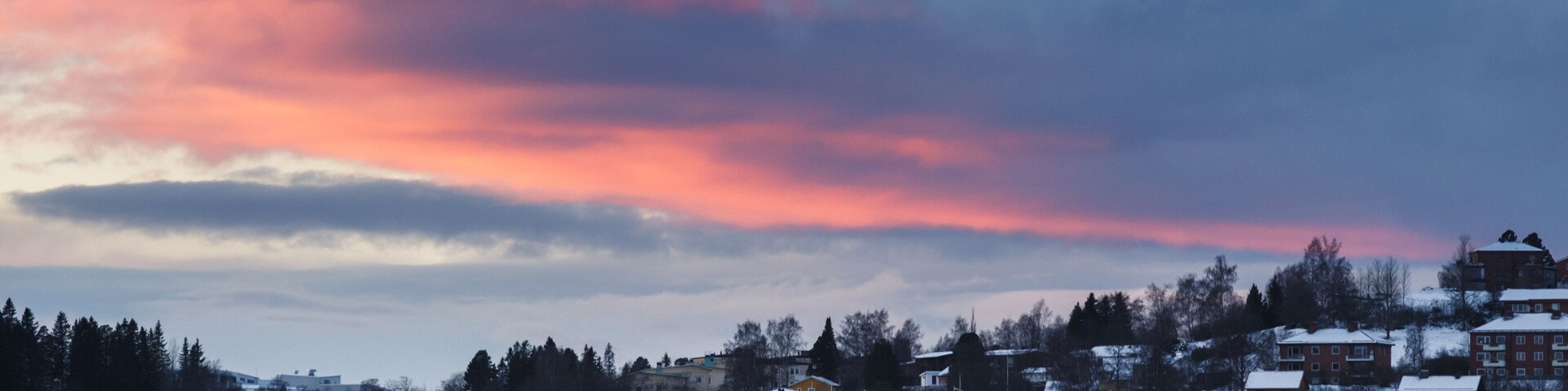 Zona residencial nevada con casas y árboles bajo un cielo con colores del atardecer.