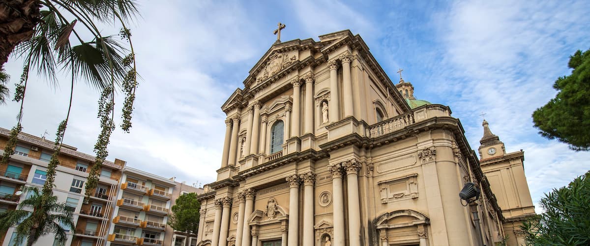 A historic church with a large dome and columns, surrounded by modern buildings and palm trees.