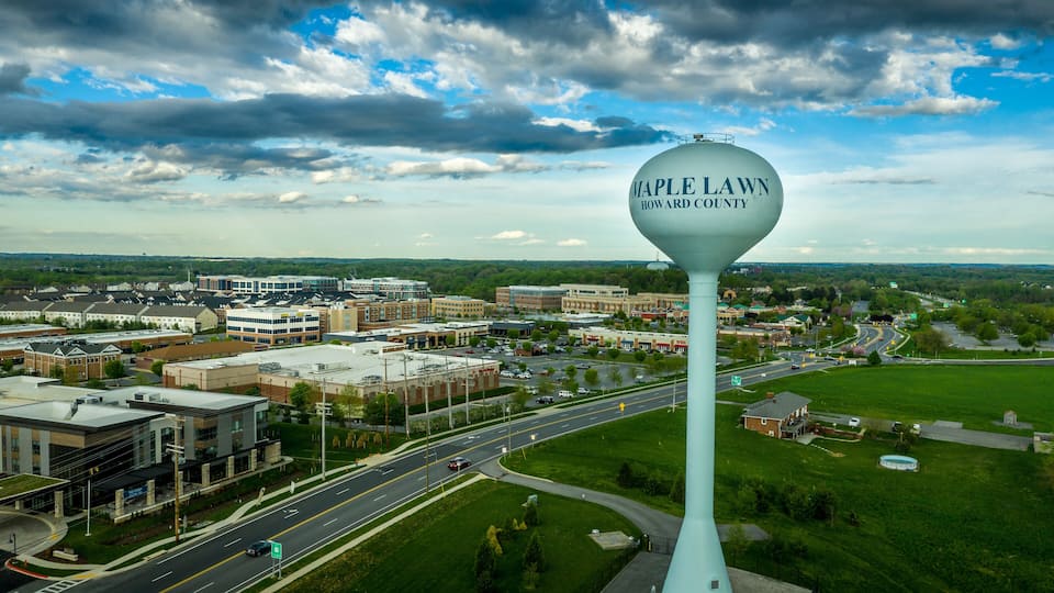 A water tower with "Maple Lawn Howard County" written on it, surrounded by a cityscape with buildings and roads.