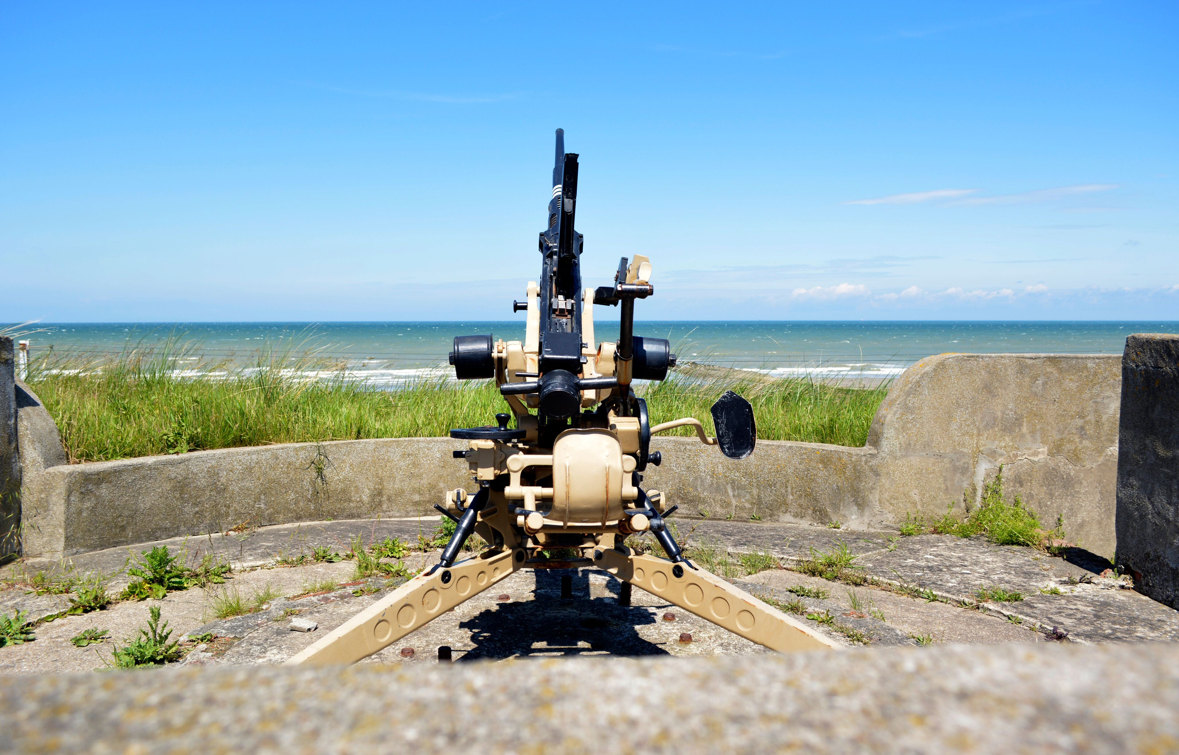 A mounted machine gun on a concrete platform overlooking the ocean.